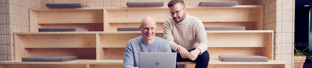 Image of two people working on a laptop in an informal office setting.