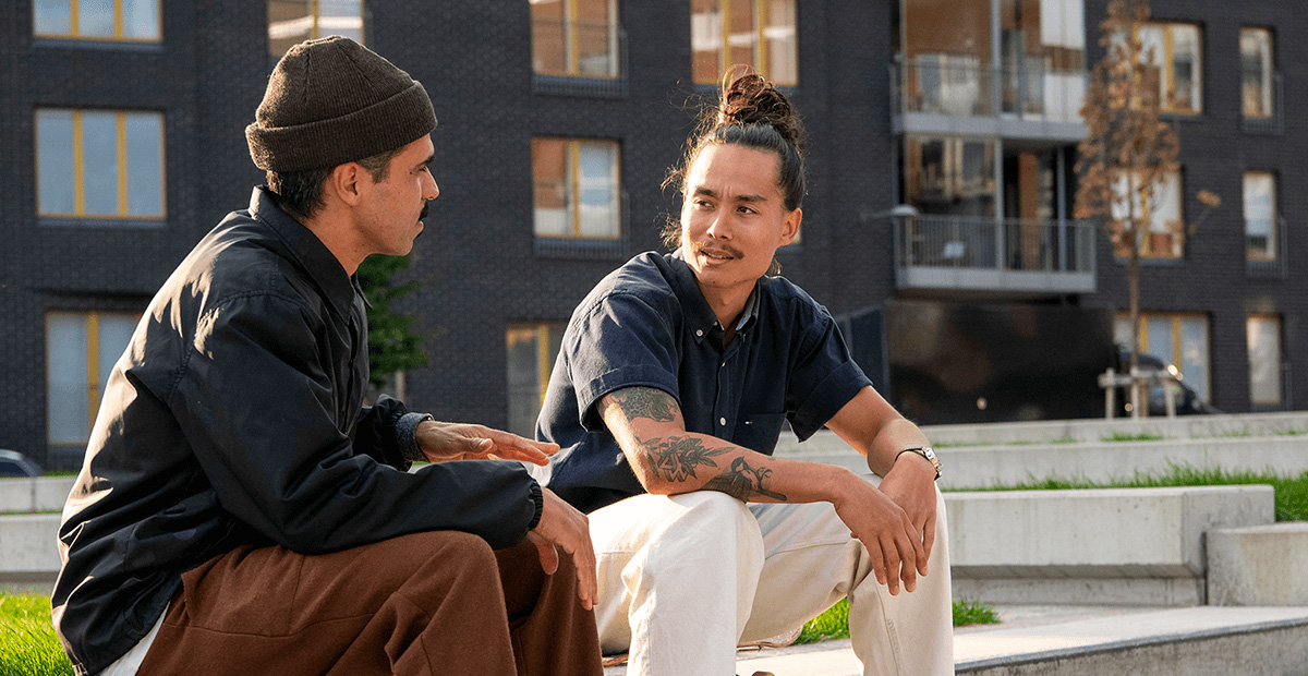 Decorative image of two men in casual clothing discussing outside modern residential buildings.