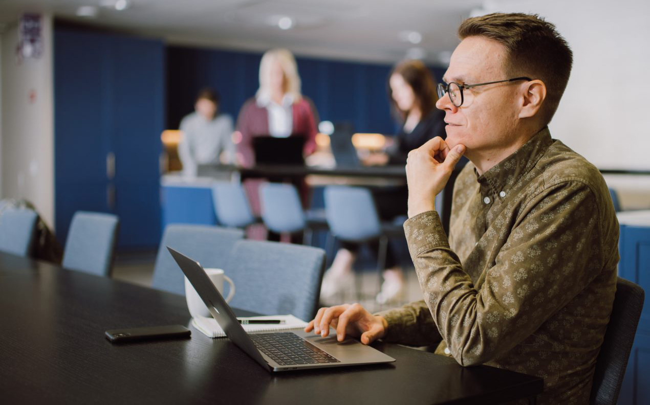 Illustration photo - Job interview in the Nordics. Man standing at a desk, with a laptop in front of him and preparing for a job interview.