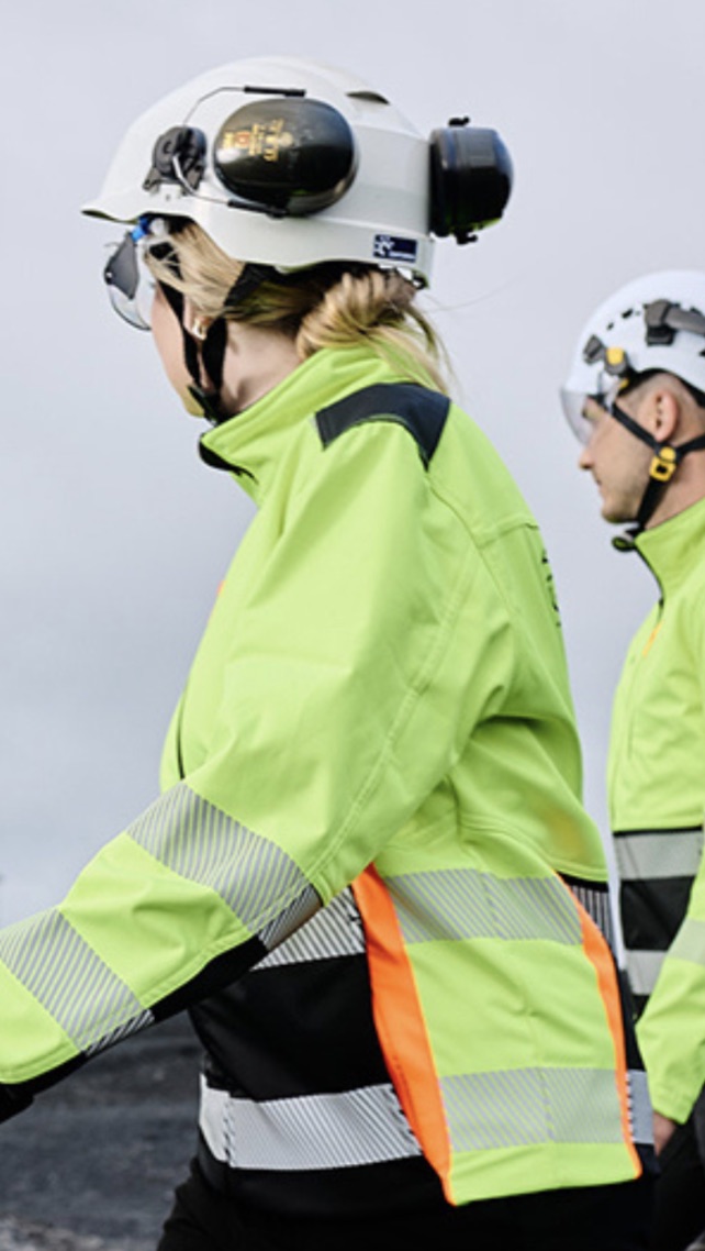 two people in reflective yellow jackets walking with helmets and hearing protection for construction sites