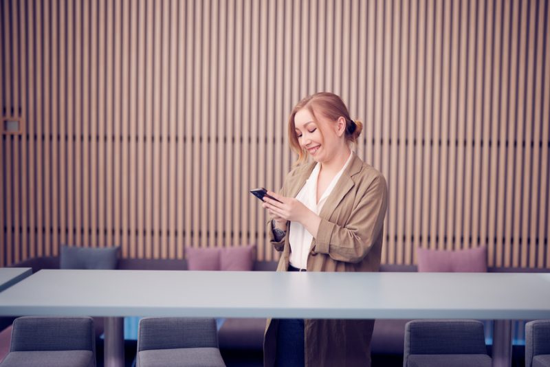 En kvinna står vid ett bord med en mobiltelefon.