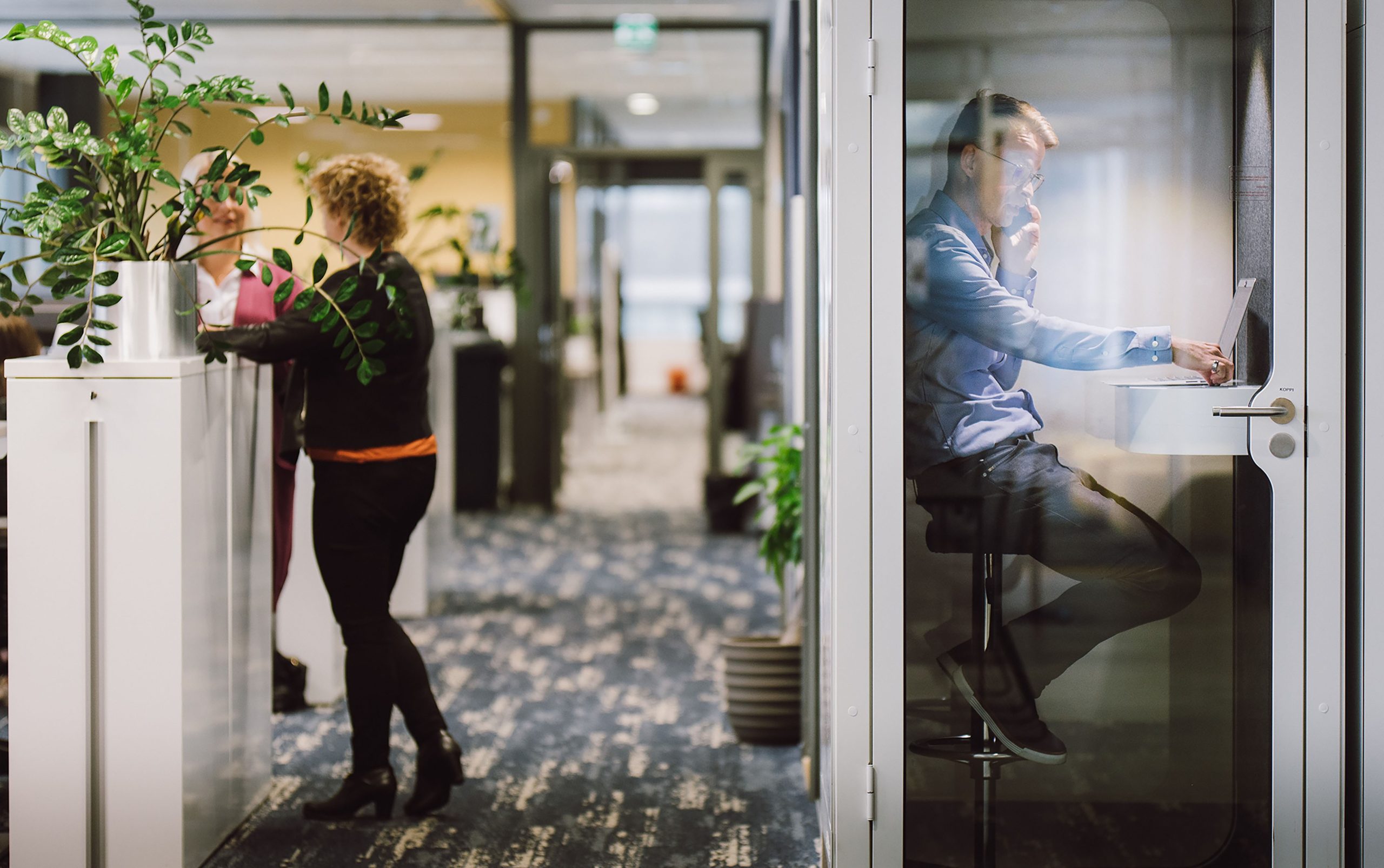 Dekorativ bild av två personer som samtalar i ljus kontorskorridor, betonar teamwork.