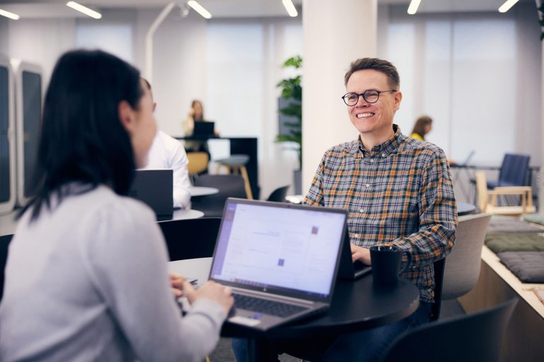 Dekorativt foto av två personer som ler och pratar på en kontorsmiljö.