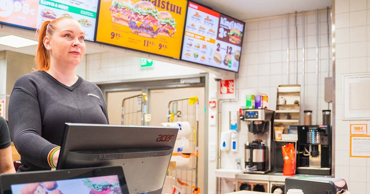 Dekorativ bild av en Burger King-anställd vid kassan med menyskyltar i bakgrunden.
