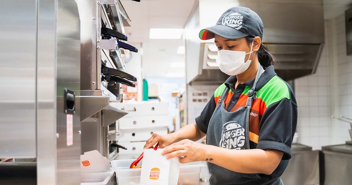 Dekorativ bild av en Burger King-anställd som förbereder mat med skyddsmask i köket.