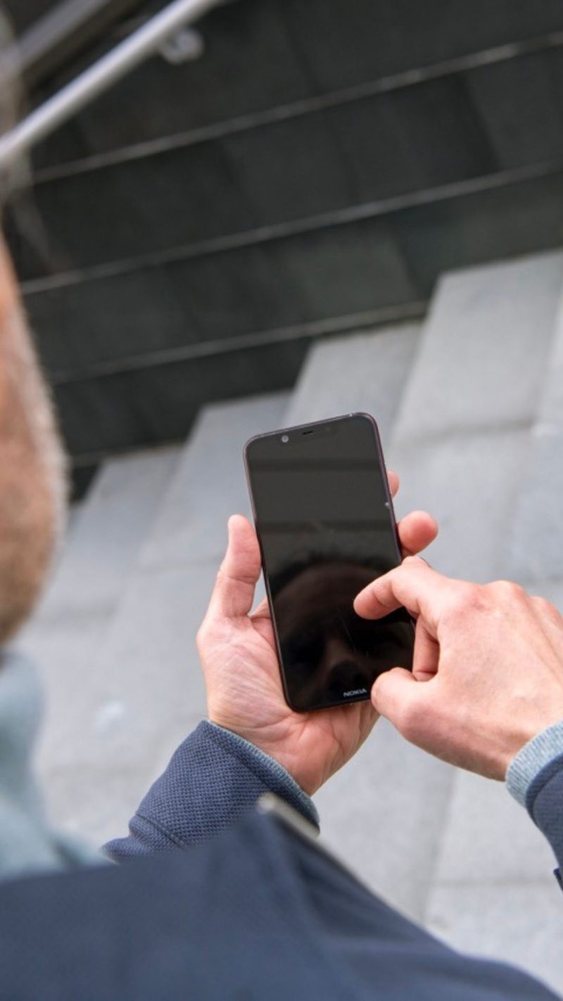 Dekorativ bild på en person i grå tröja som håller en mobiltelefon framför sig. 