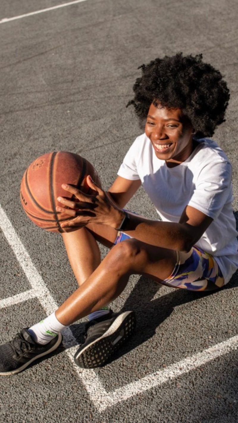Dekorativ bild på en kvinna som sitter på en basketplan med en basketboll i händerna.