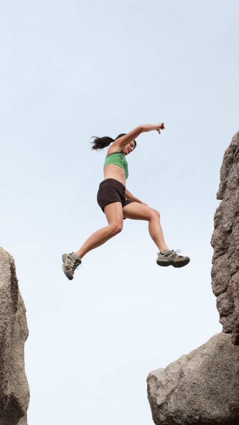 Dekorativ bild av en kvinna mitt i luften som hoppar mellan två klippformationer.