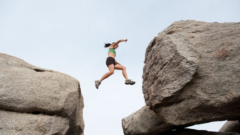 Dekorativ bild av en kvinna mitt i luften som hoppar mellan två klippformationer.