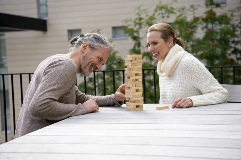 Två personer spm sitter på en blakong. Framför dem är ett bord där de spelar ett spel med träklossar