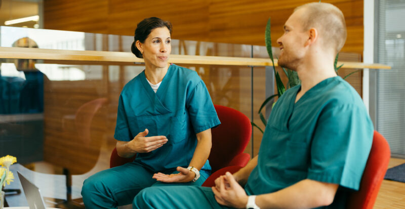 Dekorativ bild av två vårdpersonal som sitter vid ett bord och pratar med varandra.