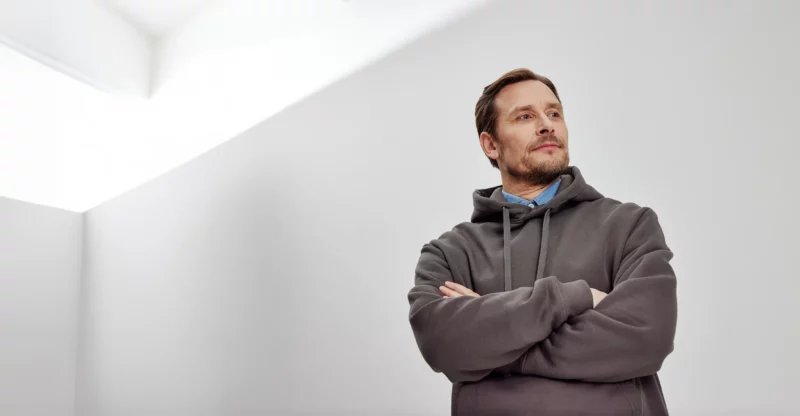 Dekorativ bild som föreställer en man i grå hoodie med armarna i kors